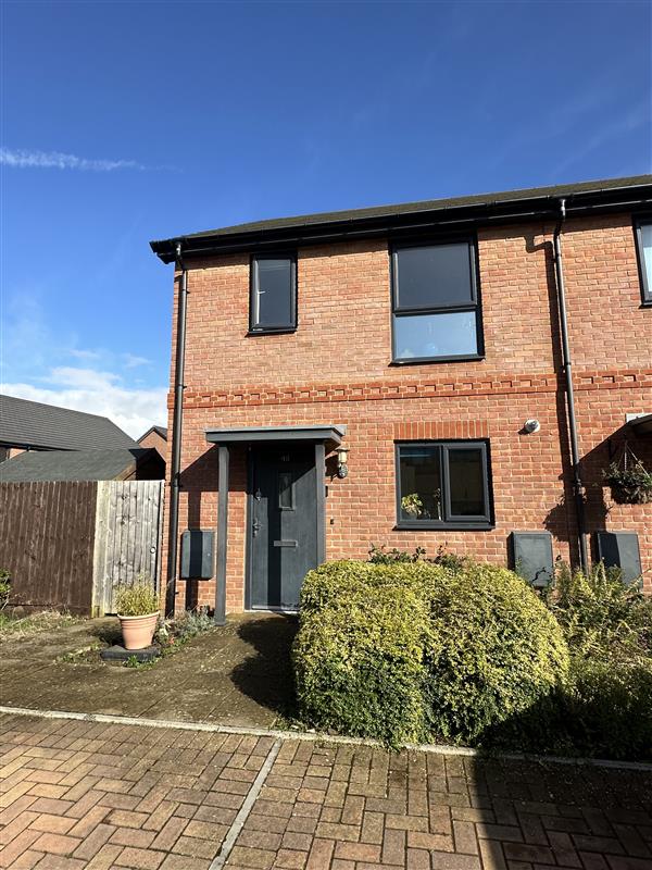 Photo of the front of 49 Caerwent Close. There is a patio and to the right of the image is a hedge. The house has red bricks and a black front door, porch and window frames.