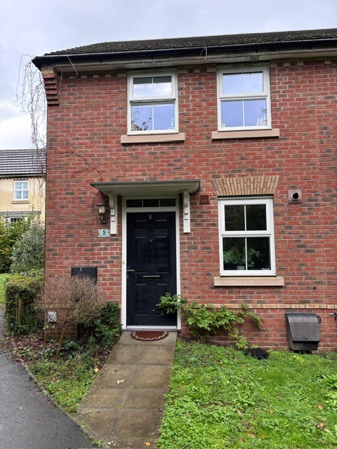 Front of red-brick house with black front door. To the right of image is a lawn and to the left of the image is a parking space